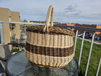 Handwoven willow market basket with a braided rim and twisted handle on a glass garden table on a sunny balcony