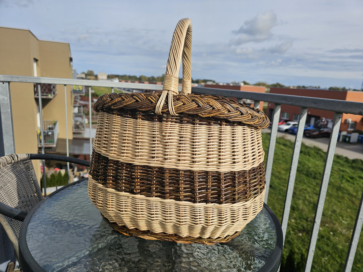 Handwoven willow market basket with a braided rim and twisted handle on a glass garden table on a sunny balcony