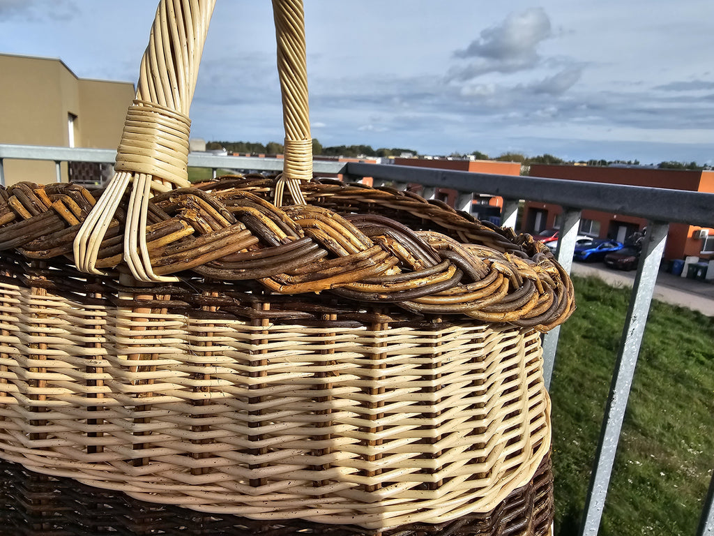 Close view of the oval willow bread basket showing the thick braided rim and the twisted handle, photographed outdoors on a balcony