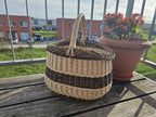 Oval wicker bread basket with a twisted handle on a wooden balcony table beside a potted flowering plant