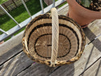 Top view into the oval willow basket on a wooden deck, showing the woven oval base, the braided rim and the twisted handle