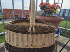 Close view of the braided rim and the twisted handle of the oval wicker basket on a balcony table beside potted begonias