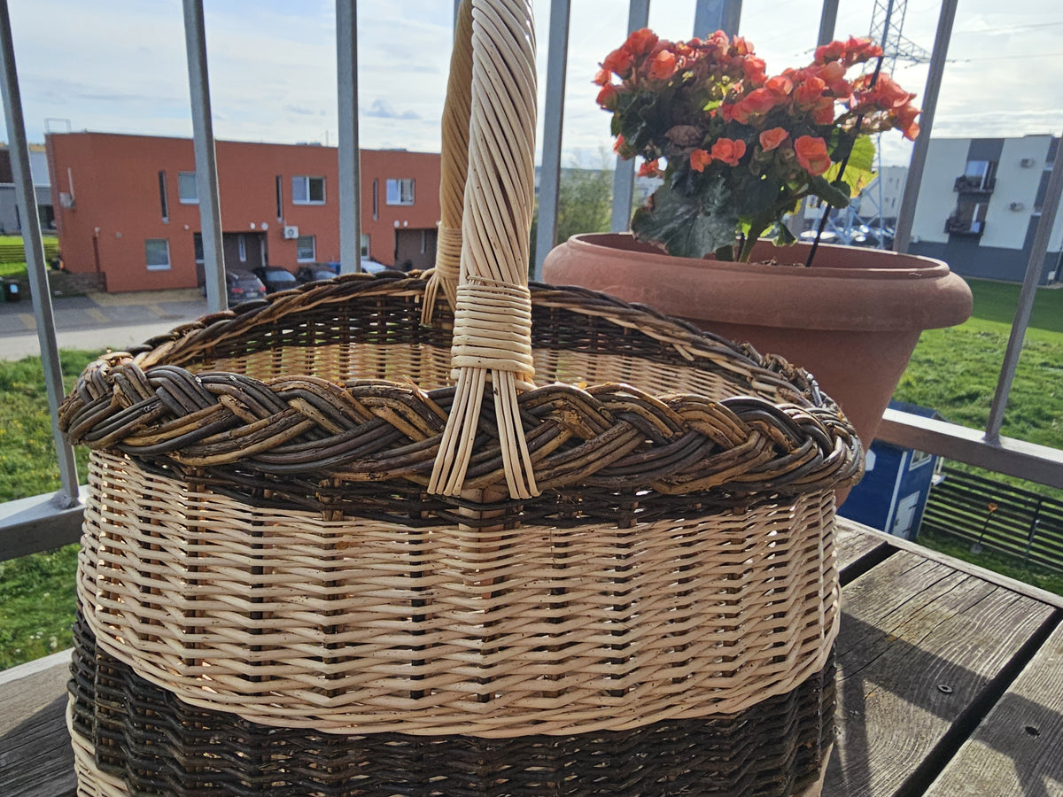 Close view of the braided rim and the twisted handle of the oval wicker basket on a balcony table beside potted begonias