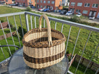 Medium oval willow basket with twisted handle on a round glass table on a balcony overlooking a lawn