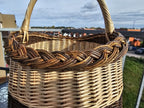 Close view of the braided rim and arched twisted handle of the handwoven willow market basket against the sky