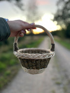 Mini round willow basket held in one hand against a sunset over a country track.