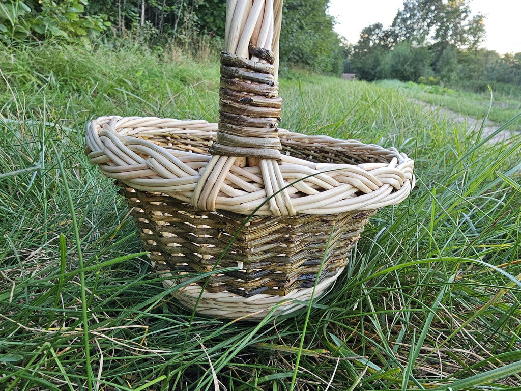 Close view of the little basket in long grass, showing the plaited rim and the bound handle.