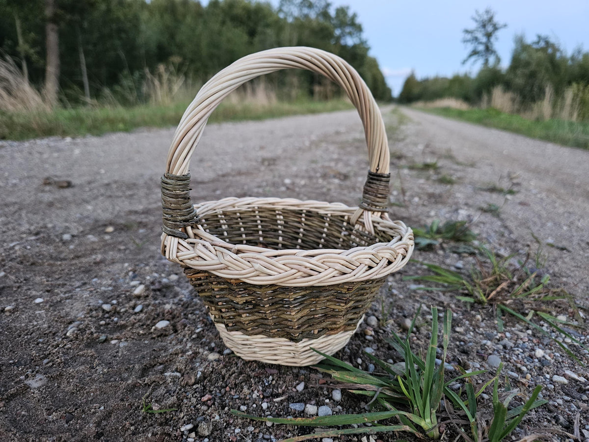 Small round flower girl basket woven from willow with a braided rim, standing on straw among strawberry plants and holding berries.