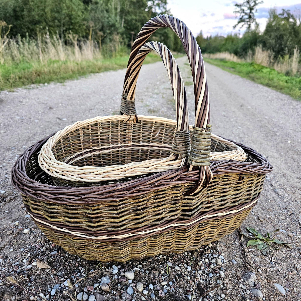 Two handwoven willow baskets on a gravel path, the smaller one resting inside the larger