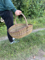 Large willow basket carried by hand along a grassy country path