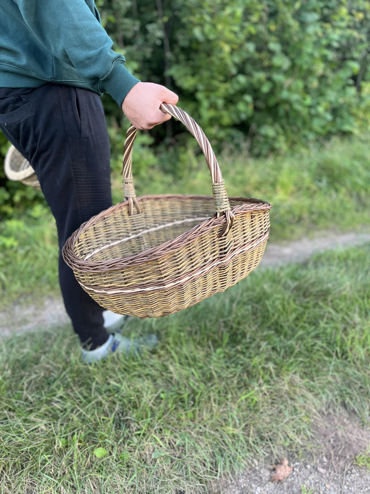 Large willow basket carried by hand along a grassy country path