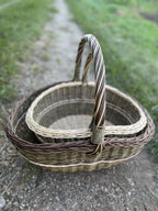 Two handwoven willow baskets on a country path, the smaller one nested inside the larger