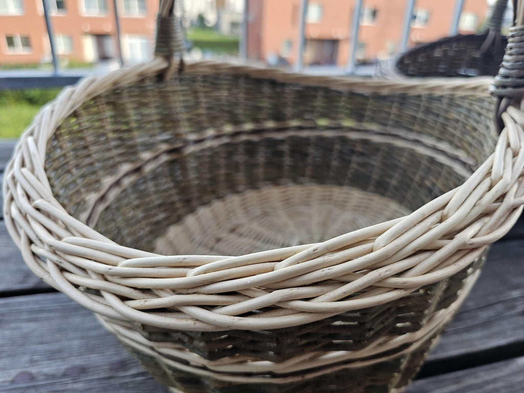 Close-up of the plaited rim and woven interior of the smaller basket from the set of two nesting willow trugs on a balcony table.