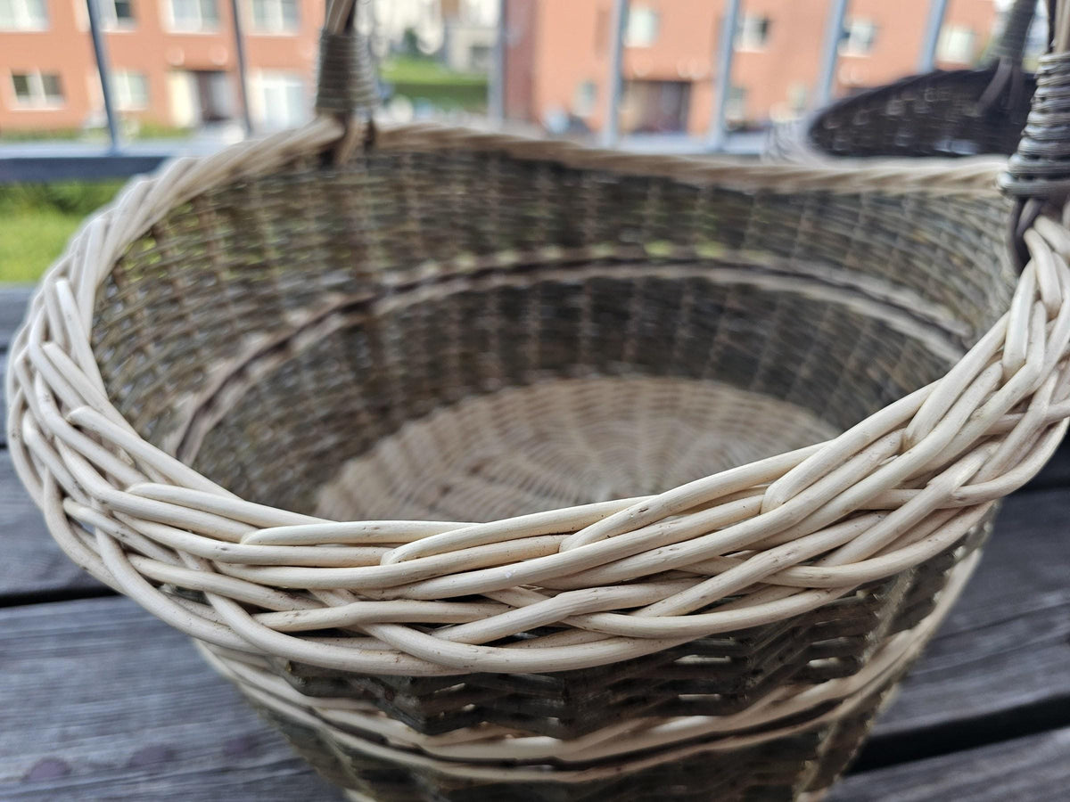 Close-up of the plaited rim and woven interior of the smaller basket from the set of two nesting willow trugs on a balcony table.