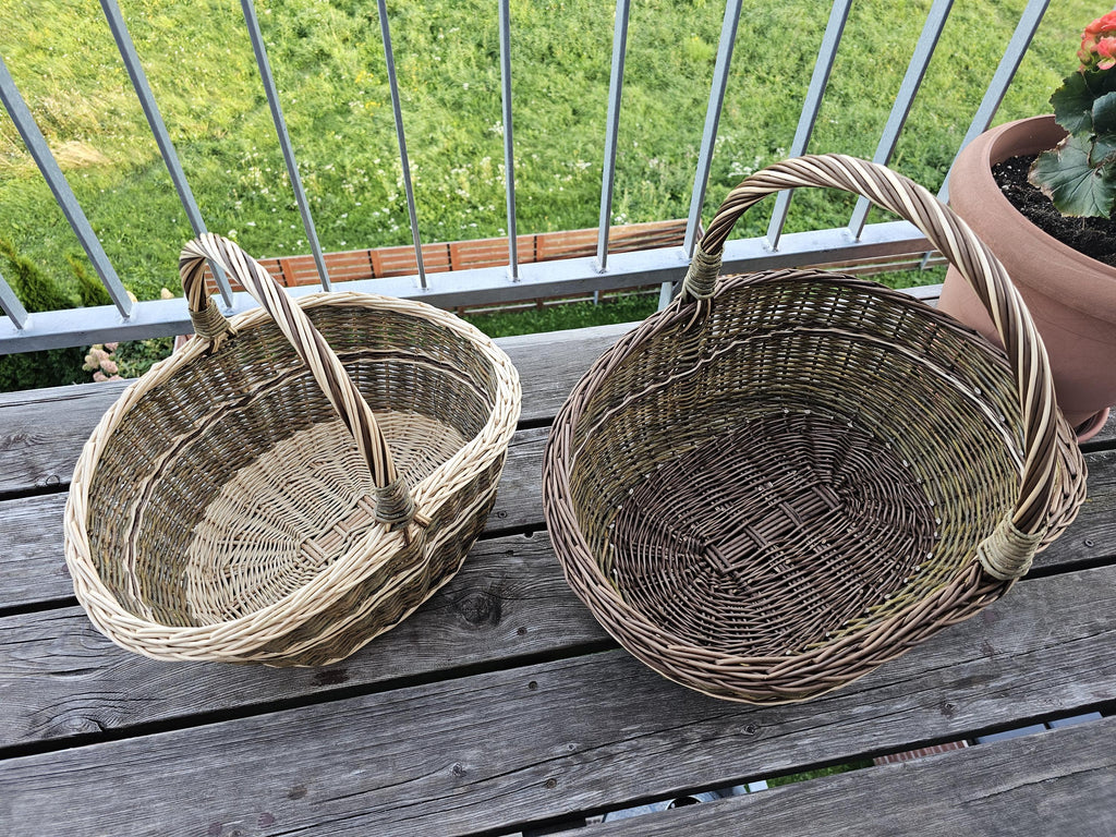 Set of 2 handwoven willow baskets side by side on a wooden balcony table, seen from above to compare their size and woven bases.