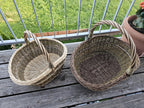 Set of 2 handwoven willow baskets side by side on a wooden balcony table, seen from above to compare their size and woven bases.