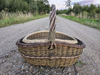 Set of 2 nesting wicker baskets on a long gravel road, the smaller trug sitting inside the larger with both twisted handles upright.