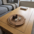Round openwork willow tray on a wooden coffee table in a living room, holding pine cones and two tealight candles as table decor.