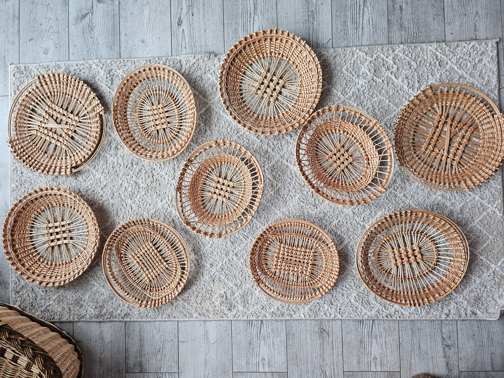 Ten handwoven openwork willow trays with different patterns laid out together on a rug
