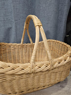 Close-up of the two arched handles bound together at the top of the oval wicker market basket, above its woven rim