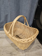 Oval willow basket with two arched handles fixed to each side, showing the deep woven interior from above on a wooden floor