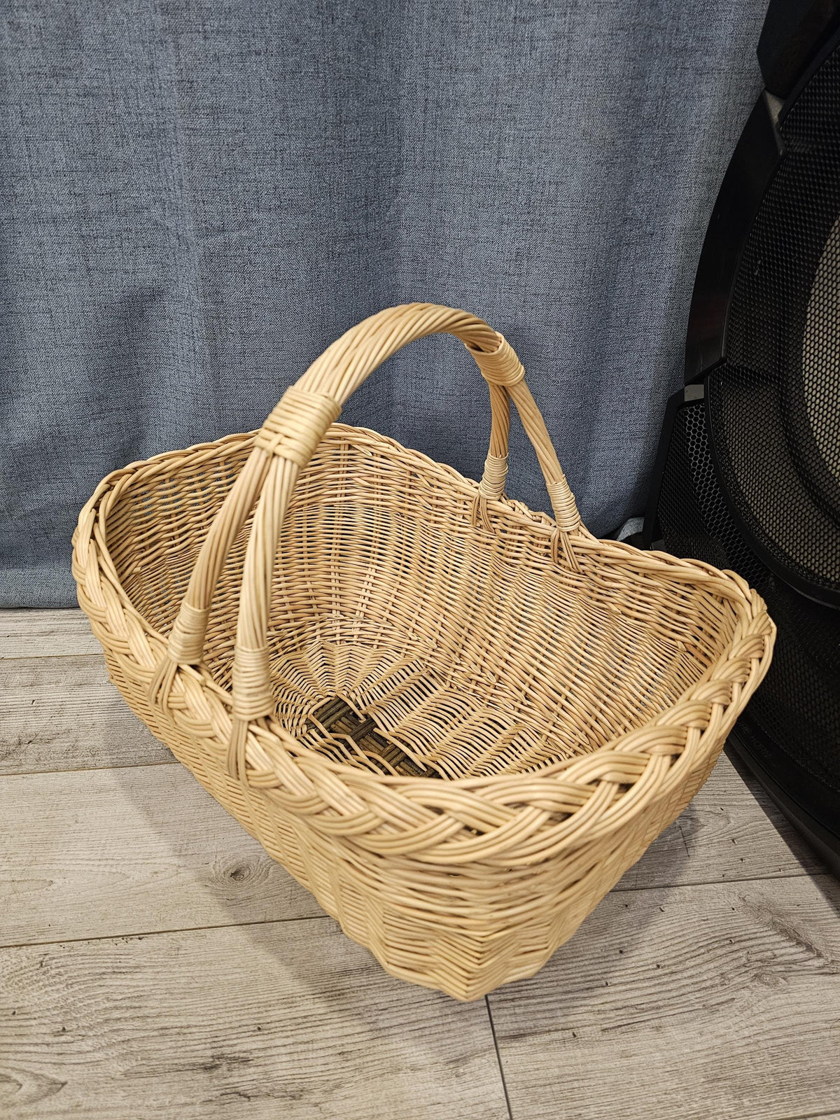 Oval willow basket with two arched handles fixed to each side, showing the deep woven interior from above on a wooden floor