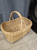 Empty oval willow market basket with rounded corners and two curved handles attached at the sides, on a light wooden floor