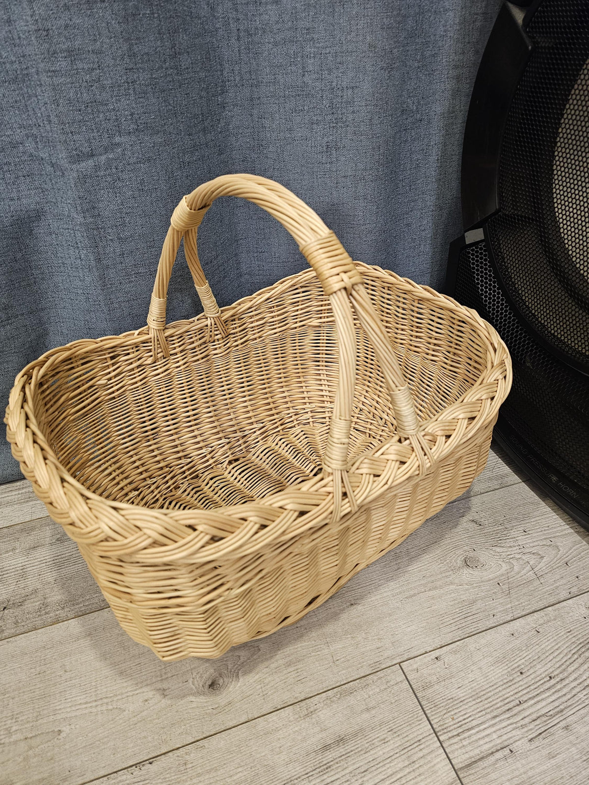 Empty oval willow market basket with rounded corners and two curved handles attached at the sides, on a light wooden floor