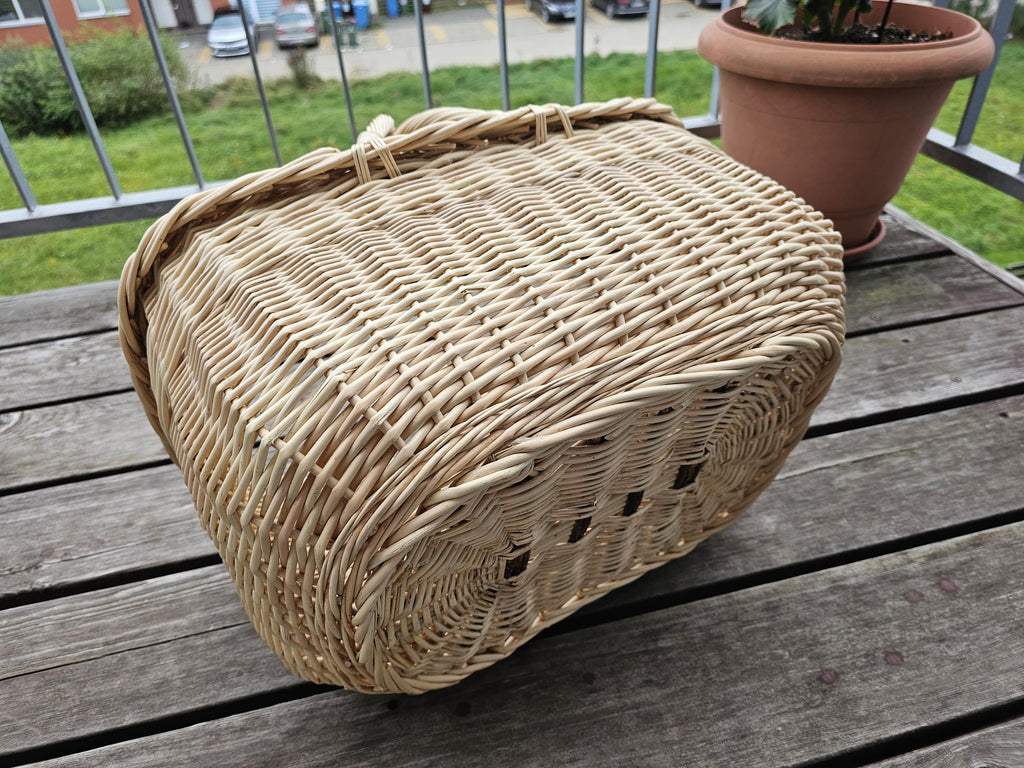 Underside of the large oval willow market basket turned upside down on a wooden table, showing the sturdy woven base