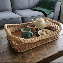 Rechteckiges Serviertablett aus Weide mit Zopfrand und Holzboden, darauf Teekanne, Becher mit Kakao und Kekse, auf dem Couchtisch am Sofa