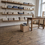 Large rectangular willow storage basket with rolled wool blankets on the wooden floor of a home goods shop