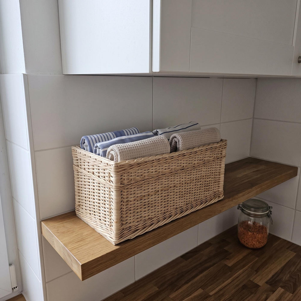 Narrow willow storage basket with folded tea towels on a wooden kitchen shelf