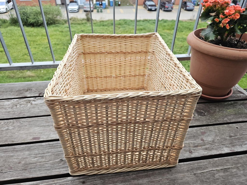 Large rectangular willow storage basket, 45 × 35 × 32 cm, handwoven from peeled willow with a thick plaited rim and raised woven bands, on a wooden balcony table.