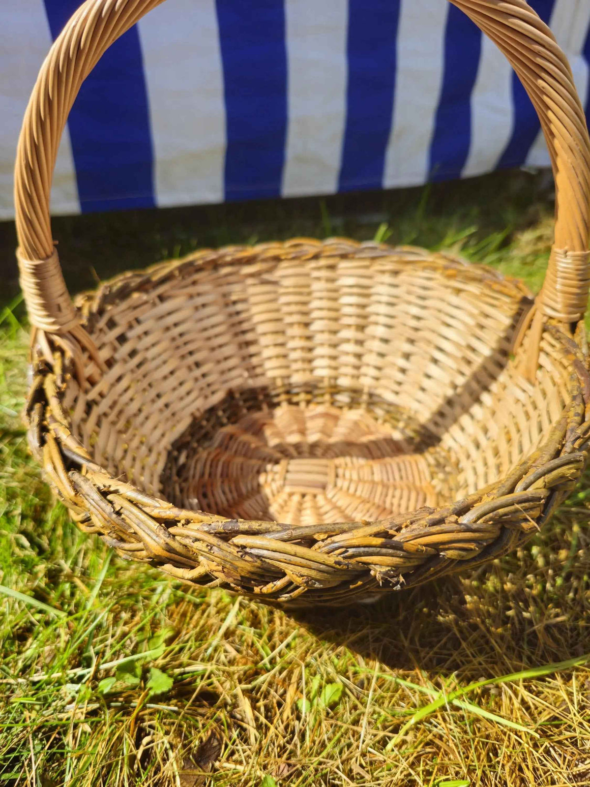 Close view into the small round willow basket on the grass, showing the woven base, the braided rim and the handle