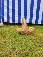 Rounded willow tray with a woven handle set low on a bed of green grass, styled outdoors against a blue and white striped cloth.