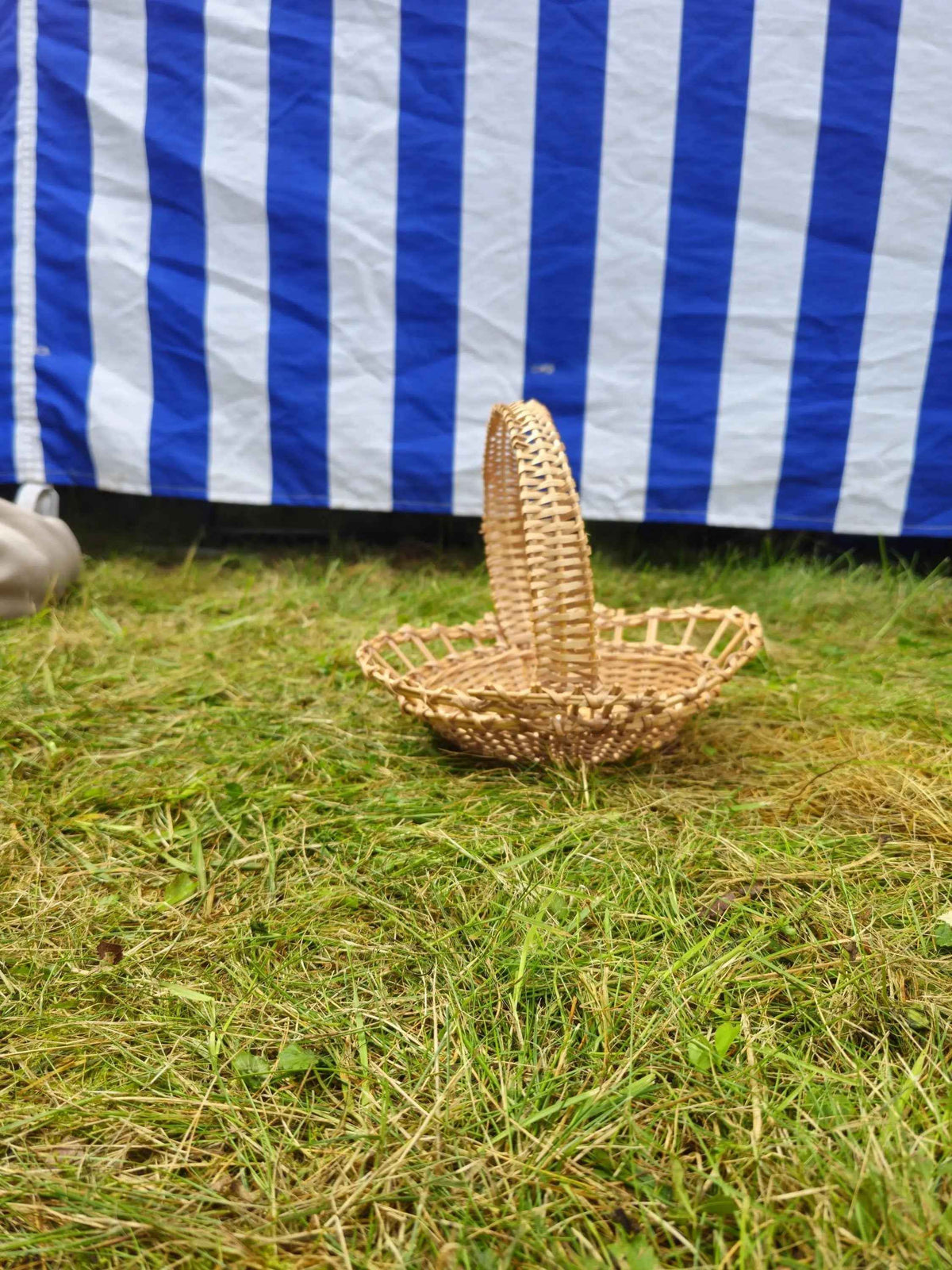 Rounded willow tray with a woven handle set low on a bed of green grass, styled outdoors against a blue and white striped cloth.