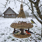 Willow bird feeder with a snow-covered bell roof hanging from a tree in winter, with great tits and a bullfinch on the platform