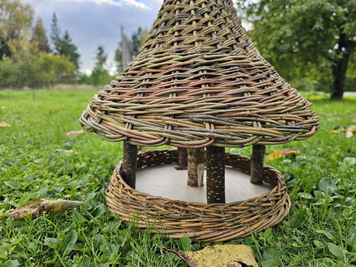 Close view of the willow bird feeder showing the branch posts holding the bell roof above the round platform with a woven rim