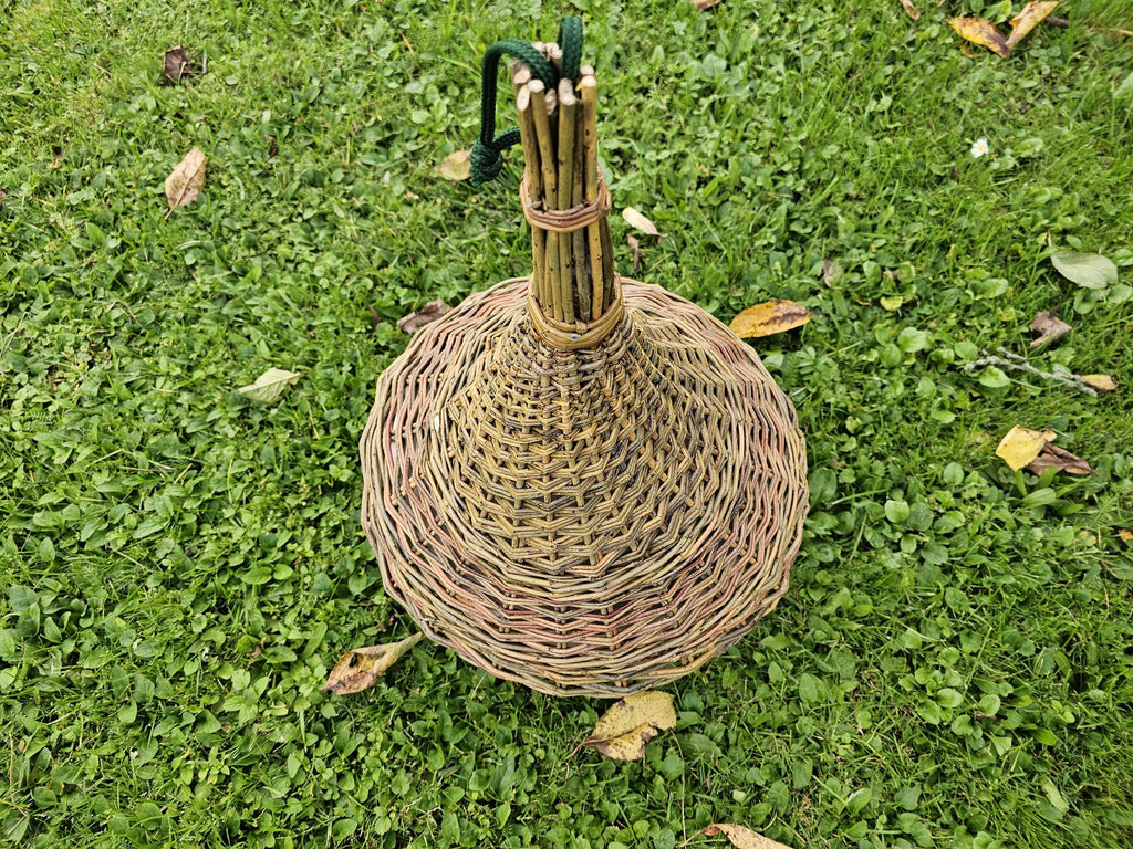 Top view of the woven bell-shaped roof of the willow bird feeder lying on grass, showing the tied spire of willow rods