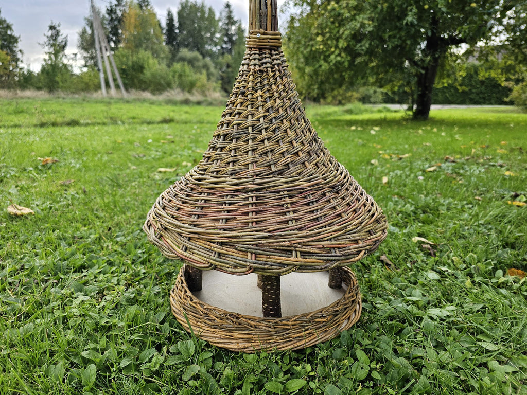 Front view of the tall willow seed station with spire top on a green lawn, the open sides visible all round