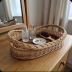 Handwoven wicker vanity tray with wooden base holding perfume bottles, rings and a hairbrush on a bedroom dresser