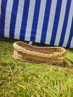 Small wicker serving tray with braided rim and raised open-weave ends resting on sunlit grass by a striped market tent