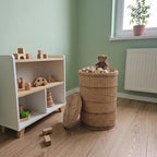 Lidded willow storage bin in a child's room holding wooden toys and a teddy bear, lid leaning against the side