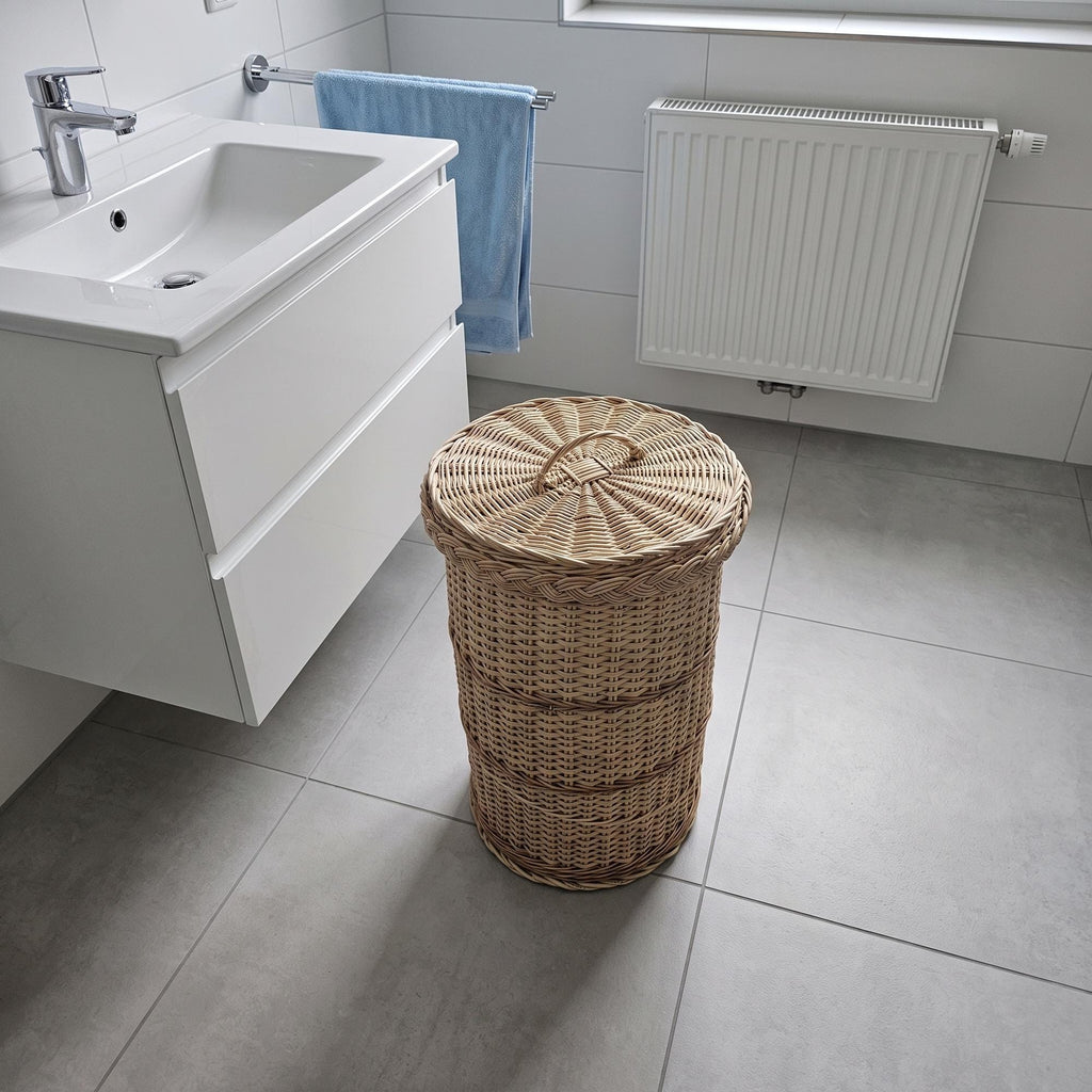 Round wicker waste bin with lid in a modern bathroom beside a white vanity unit and radiator