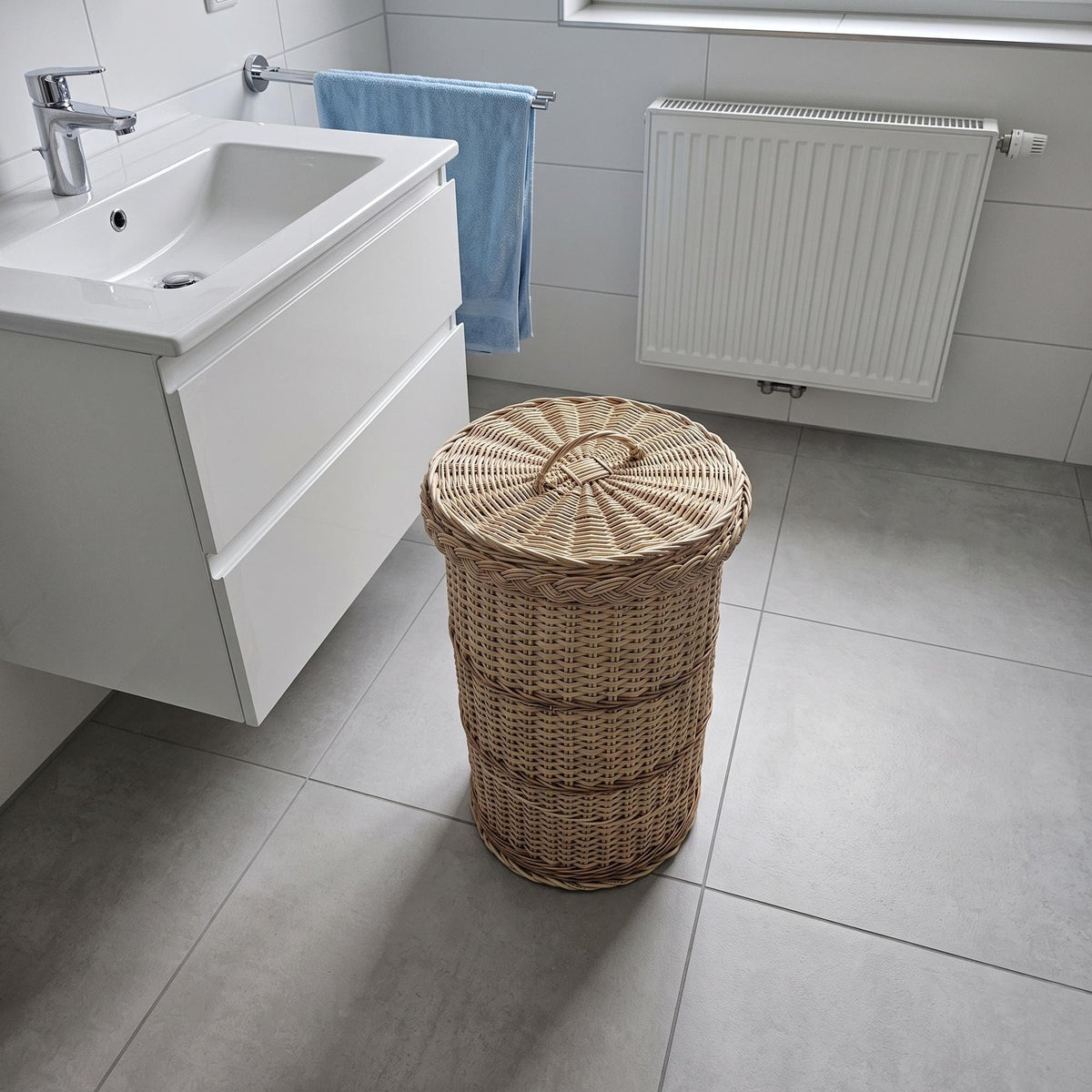 Round wicker waste bin with lid in a modern bathroom beside a white vanity unit and radiator