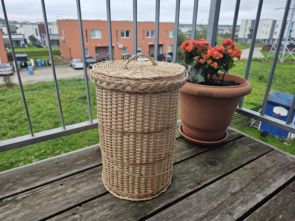 Handwoven willow trash can with lid in a three-quarter view on a wooden table